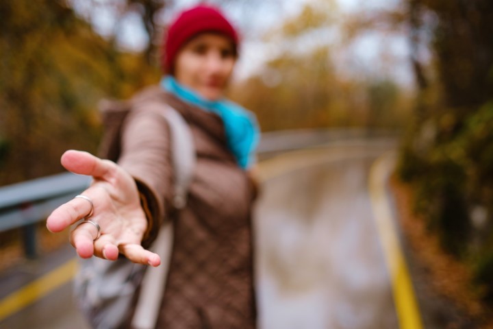 A person in a red hat reaching their hand out towards the camera in a gesture of offering help and support, with an autumn path in the background.
