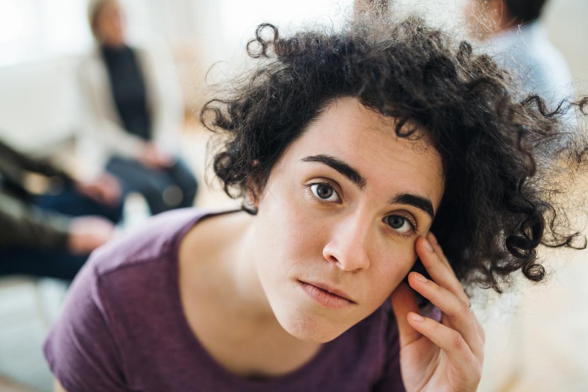  In a waiting room, a woman is captured with motion blur as she walks restlessly past other people who are sitting still, illustrating the physical symptom of hyperactivity common with ADHD.