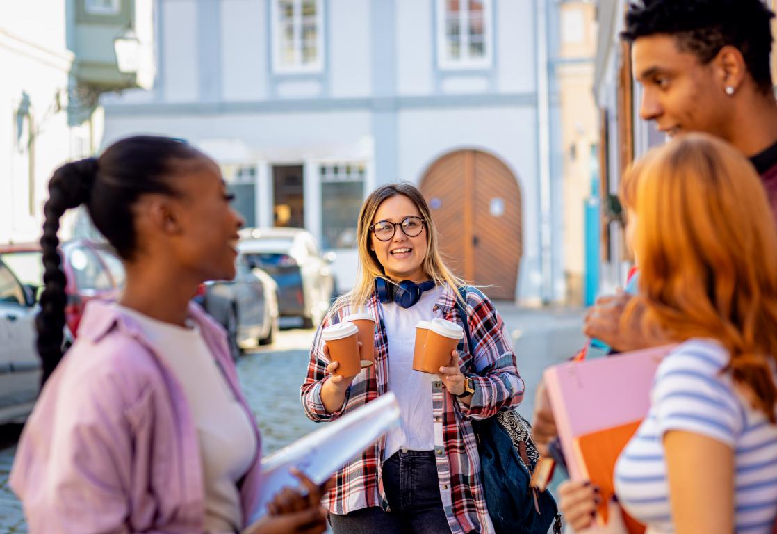 A group of four university students stand together, smiling with one student holding drinks