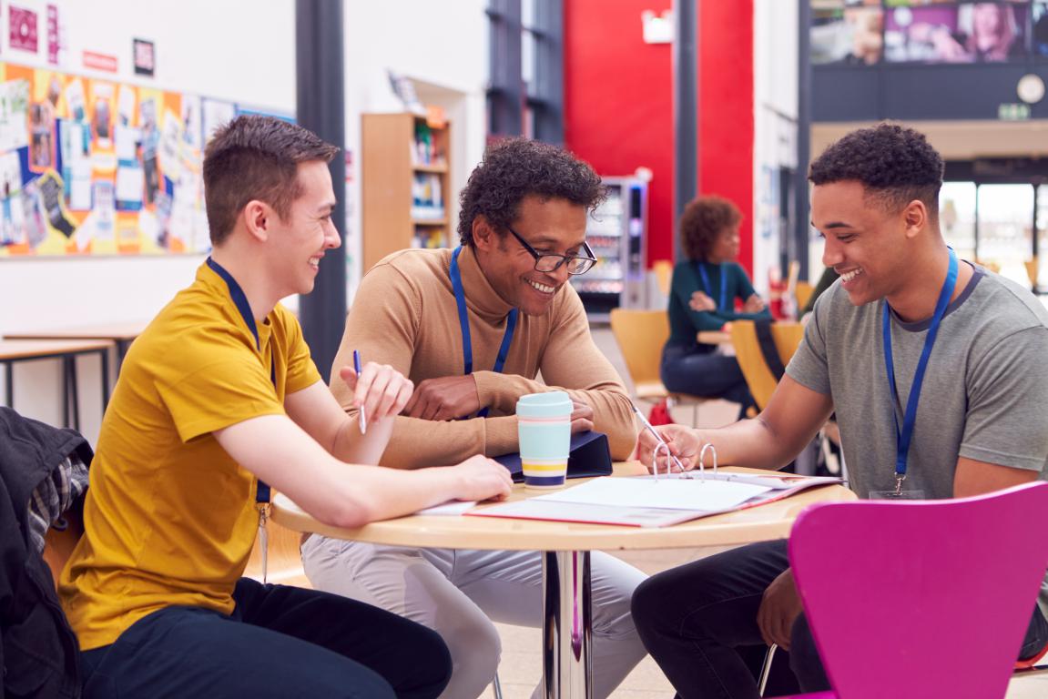  A group of three young people are sitting at a table, looking at a document and appears to be discussing it