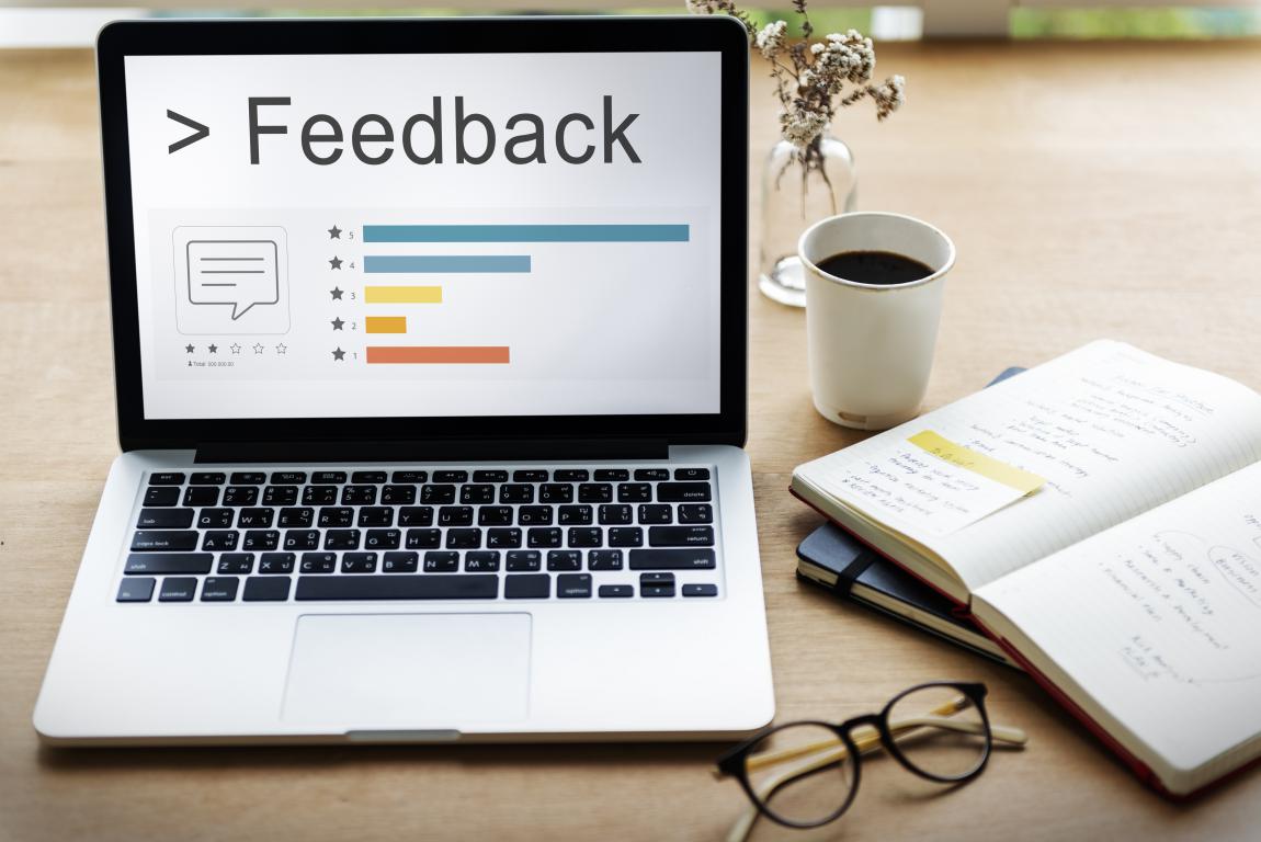 A laptop screen showing a customer feedback survey with star ratings and charts, placed on a desk with a notebook and coffee