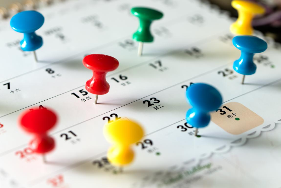 A close-up of a monthly calendar with colorful pushpins marking various dates, representing appointments and bookings.