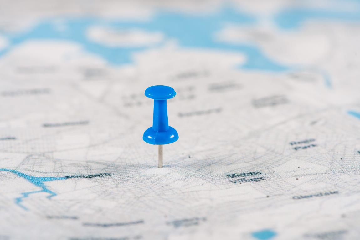 A blue pushpin pressed into a paper street map, marking a precise destination for easy navigation.