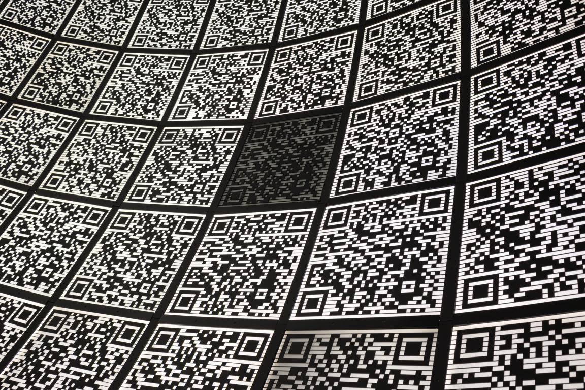  A close-up, curved wall covered in dozens of black and white QR code tiles, representing numerous digital connection points.