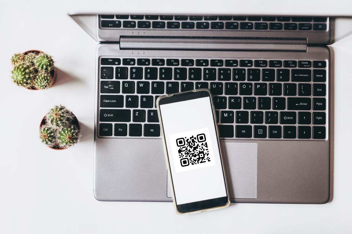 A smartphone displaying a QR code, resting on a laptop keyboard next to two small cacti
