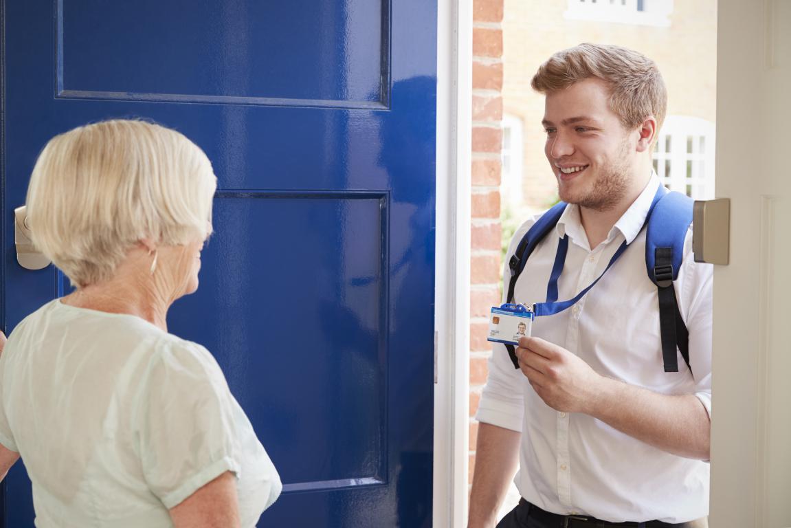  A young professional presents his photo ID card to an older female client at her front door to verify his identity and build trust.