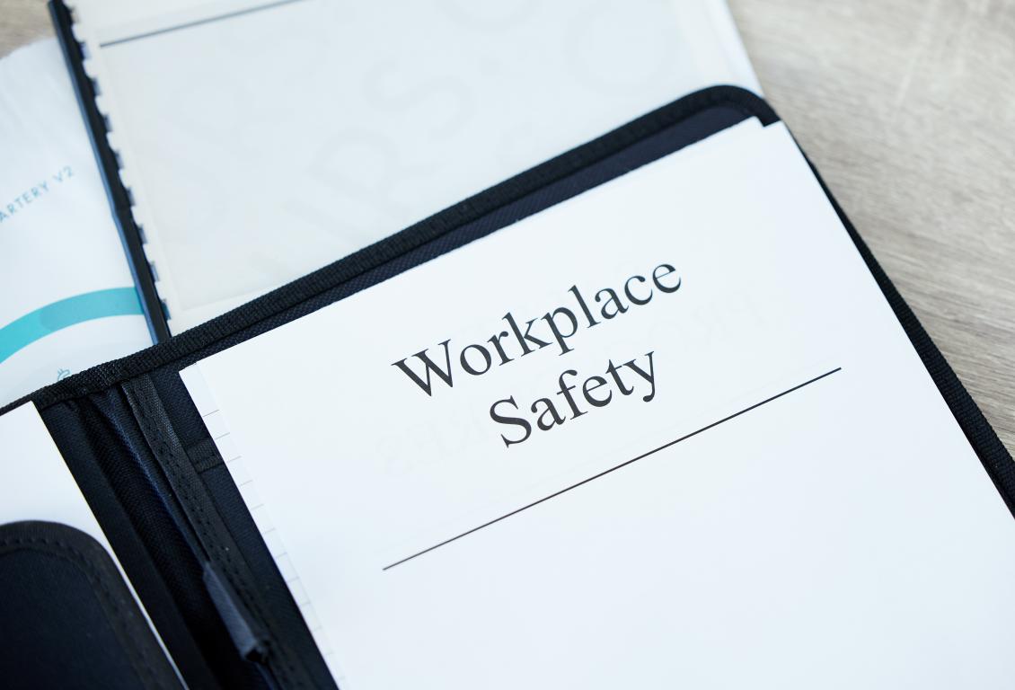  A close-up of an open black binder on a desk, with the top page clearly titled "Workplace Safety".