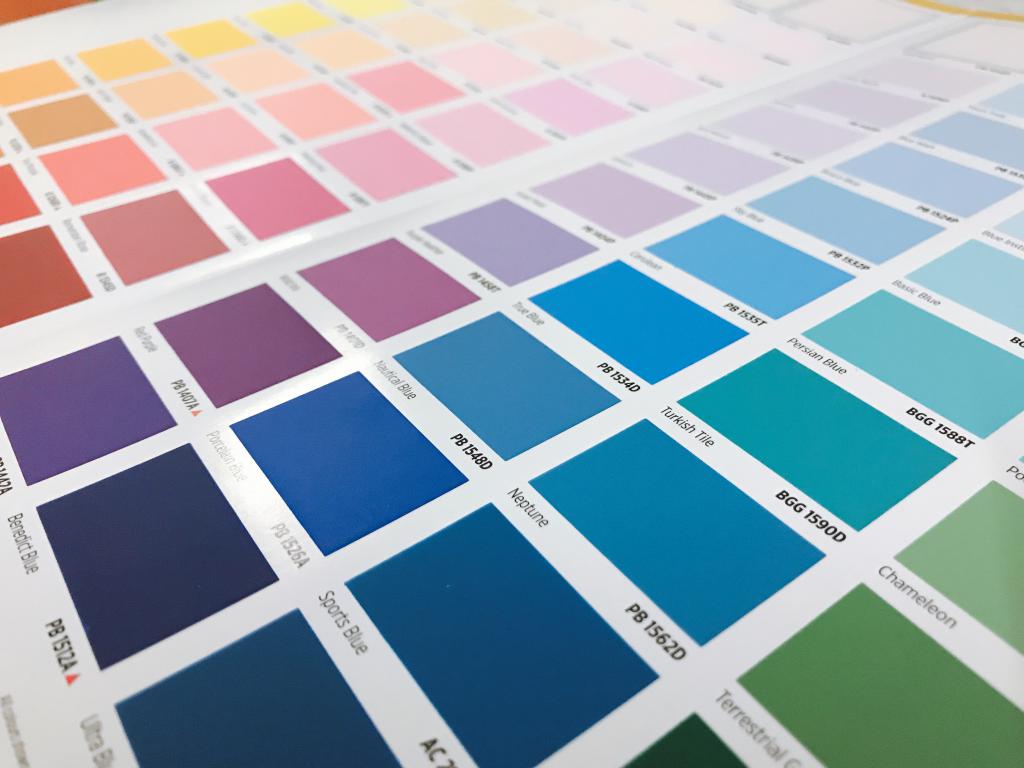 A close-up of an open colour swatch book displaying a wide variety of blue, purple, and green shades, each with a specific name and code.