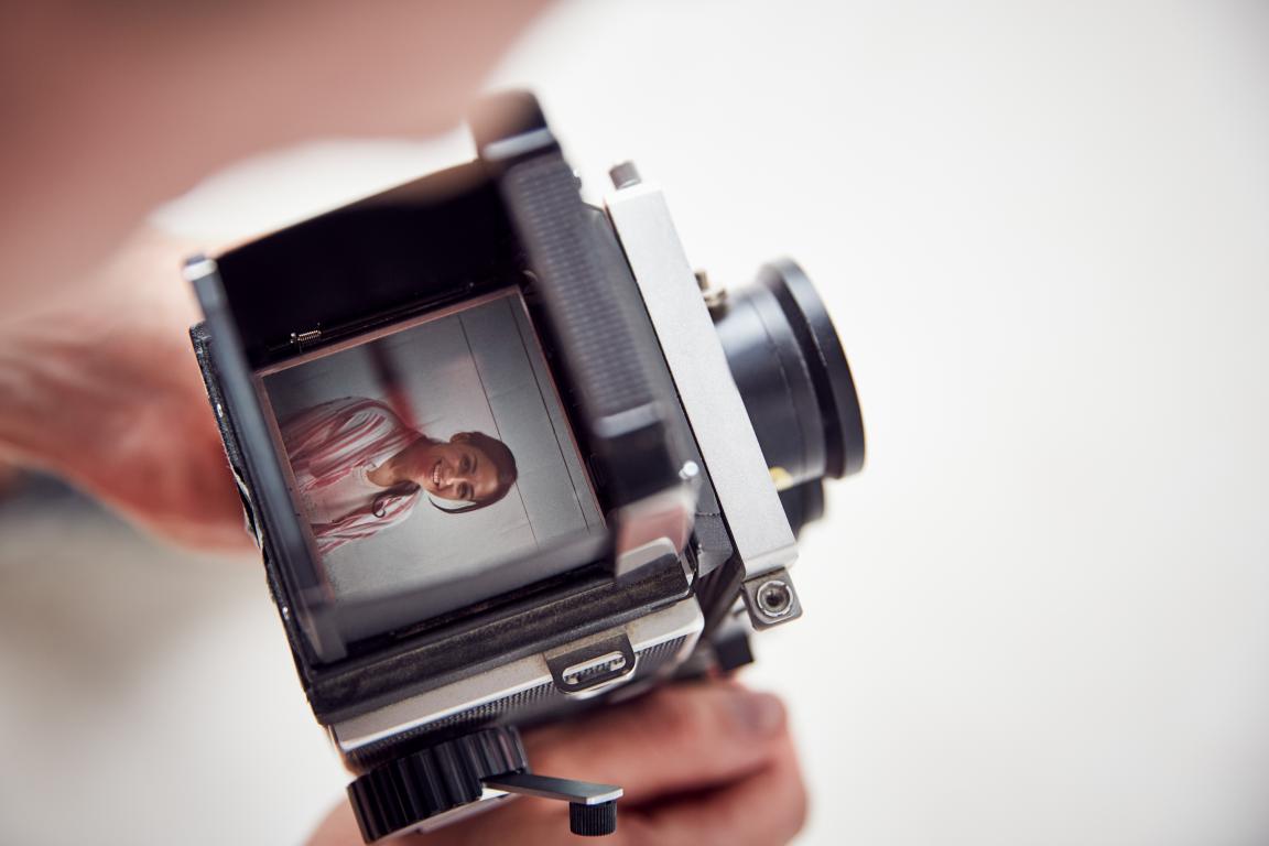 A unique view looking down into the viewfinder of a vintage camera, capturing the smiling face of a person posing for their portrait.