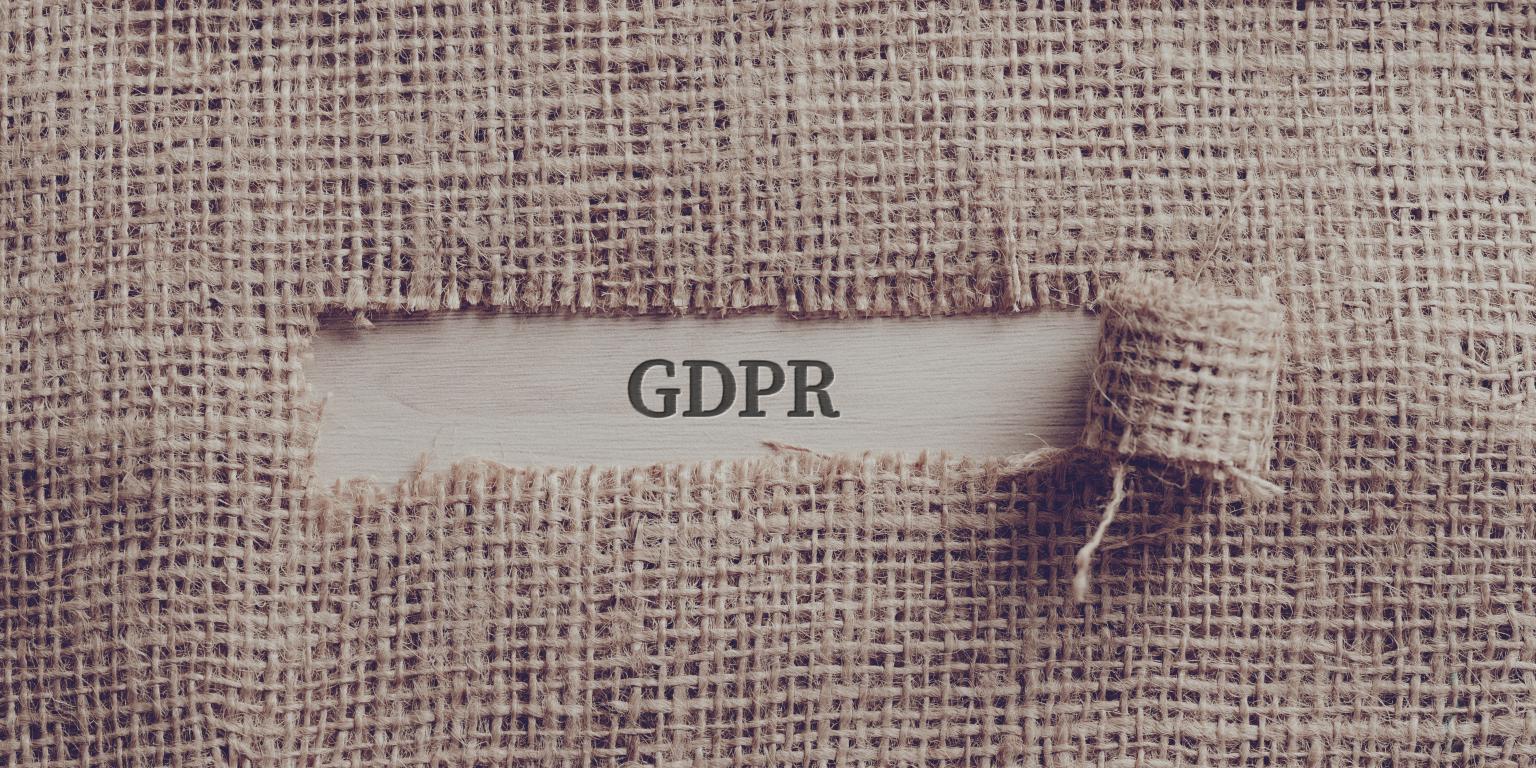  A torn piece of hessian fabric revealing the word 'GDPR' underneath, symbolizing the process of uncovering and understanding the regulations.