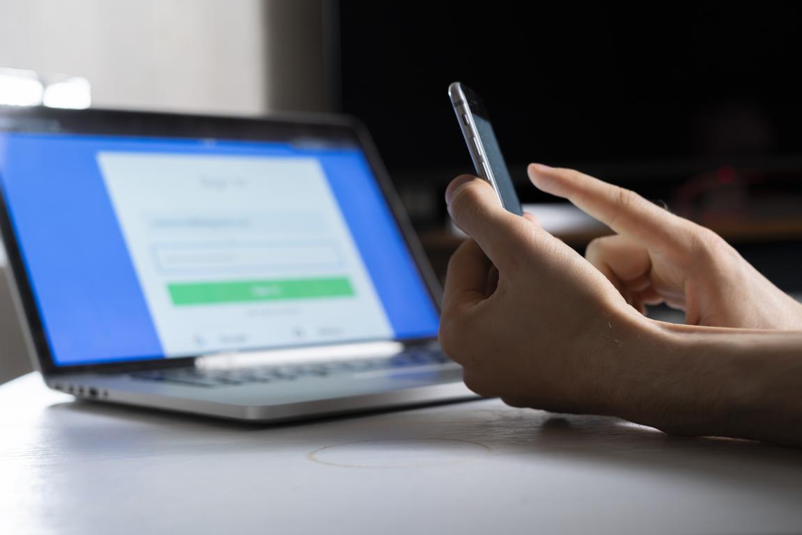 A person holds a smartphone to complete a login on a laptop, demonstrating two-factor authentication as a GDPR security measure.