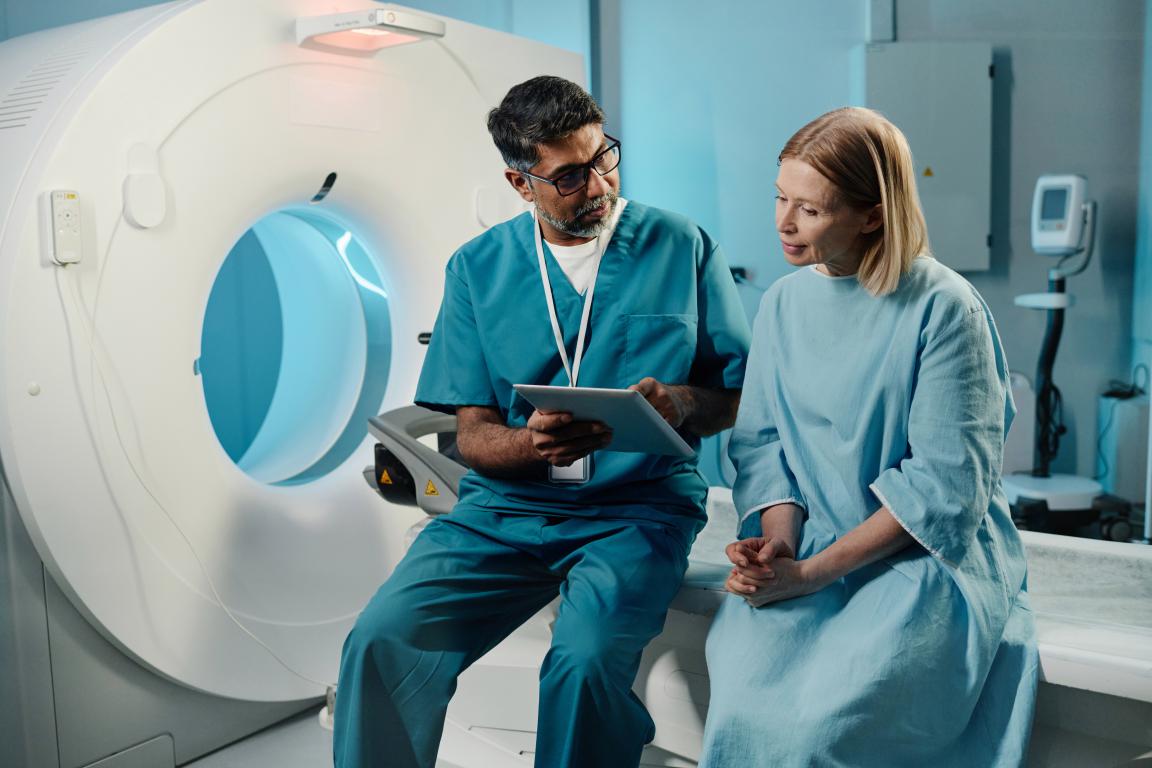 A radiographer discusses the MRI procedure with a patient, reviewing safety information on a tablet before the scan begins.