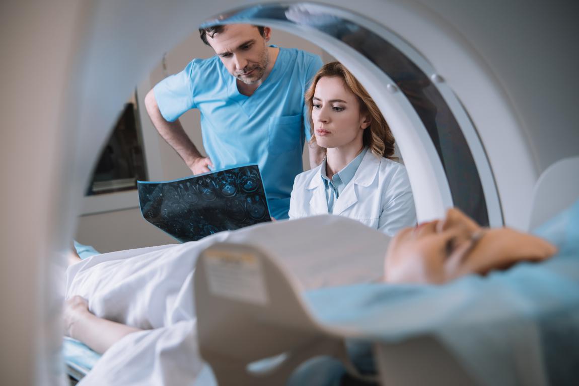 Two radiographers reviewing a diagnostic scan image next to the MRI machine while the patient lies on the bed, ensuring image quality.