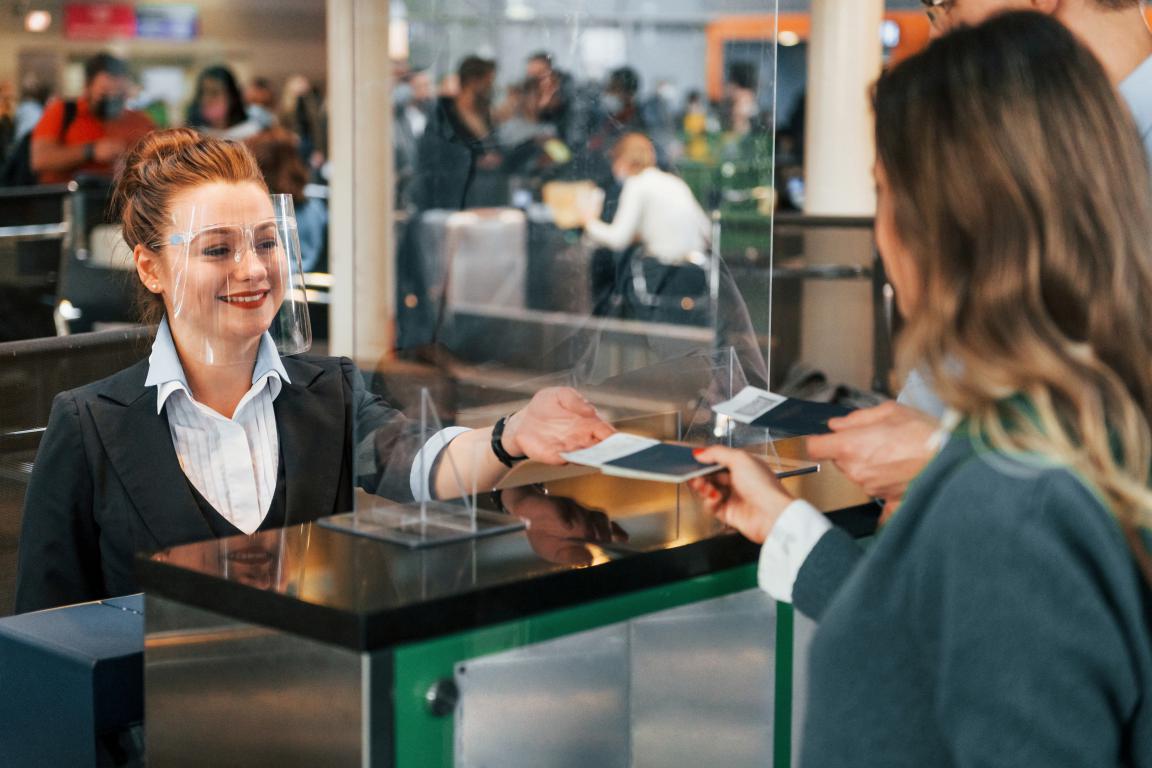 A passenger at a UK airport check-in desk presenting their passport and other travel documents to a helpful airline employee.