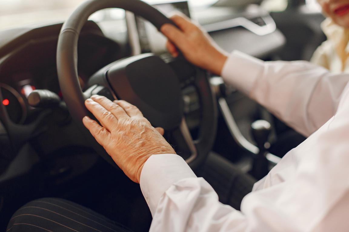 Close-up of an older person's hands holding the steering wheel, representing the desire to get back to driving after a metal implant surgery