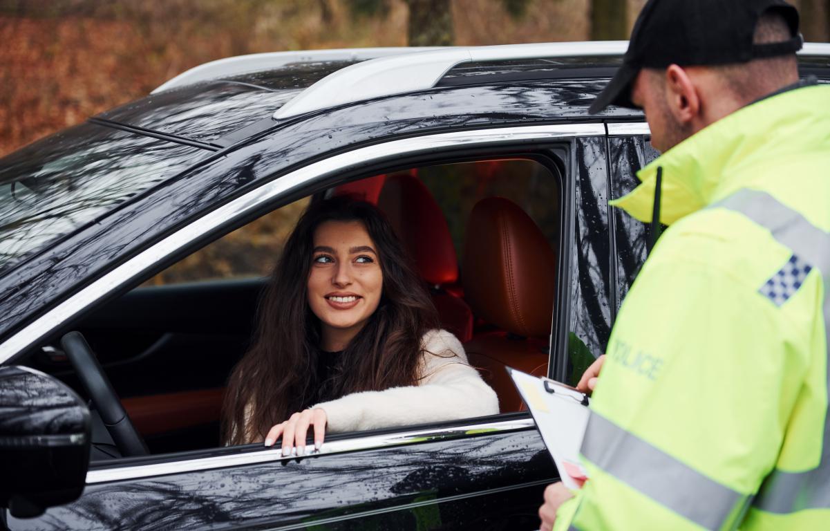 A female driver speaks calmly with a police officer during a roadside stop, highlighting the importance of being prepared with correct documentation.