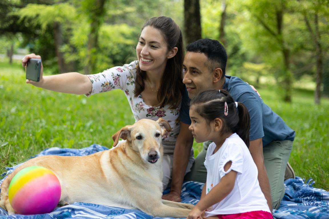 A happy family taking a selfie with their beloved dog in a park, representing the peace of mind that comes with choosing the right insurance.