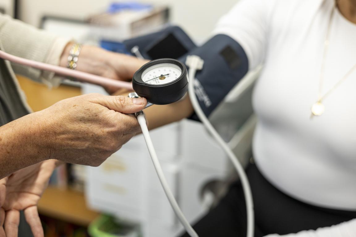 Close-up of a healthcare professional taking a patient's blood pressure using a manual cuff and gauge on their upper arm.