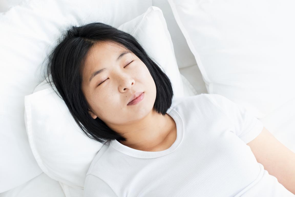A woman is sleeping peacefully in a white bed, representing a night of rest that could be affected by sleep apnea.