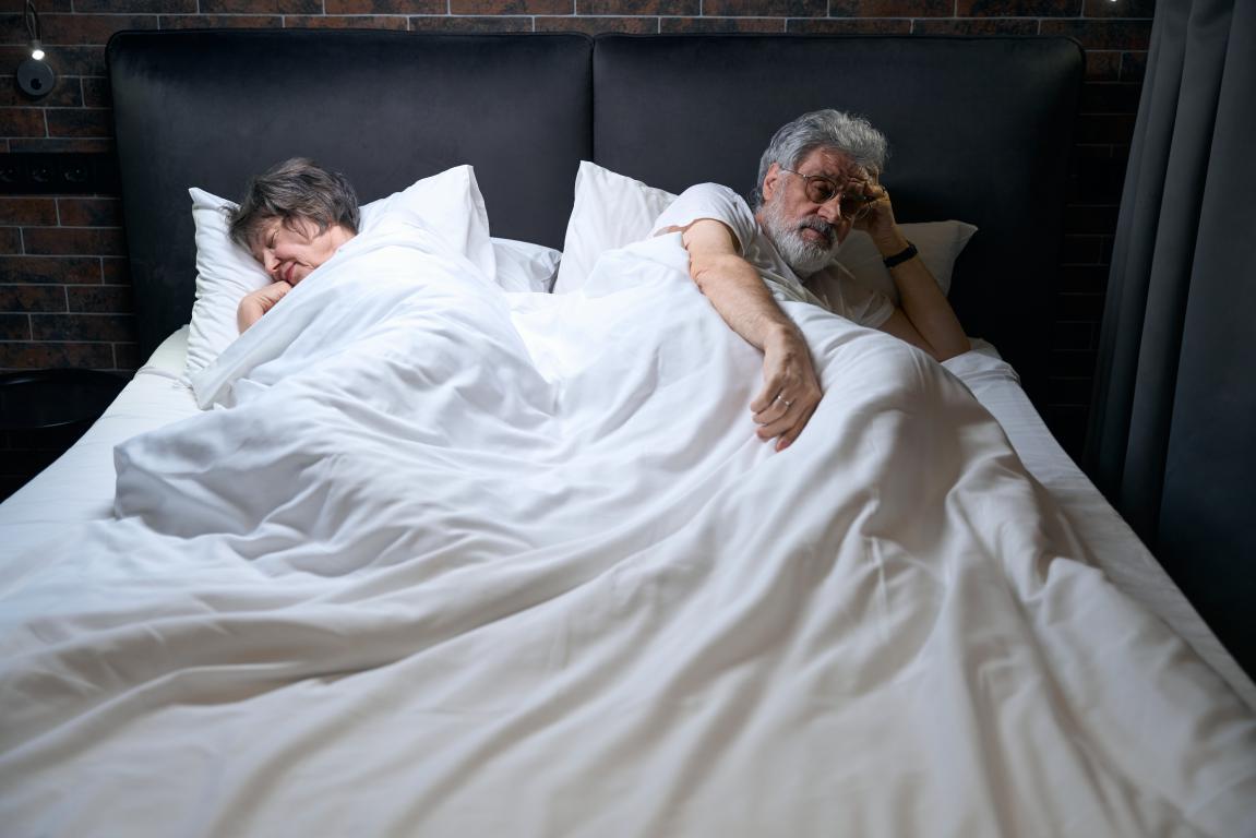 One person sleeps soundly while their partner remains awake and restless in bed, a common scenario in households affected by sleep apnea and snoring.