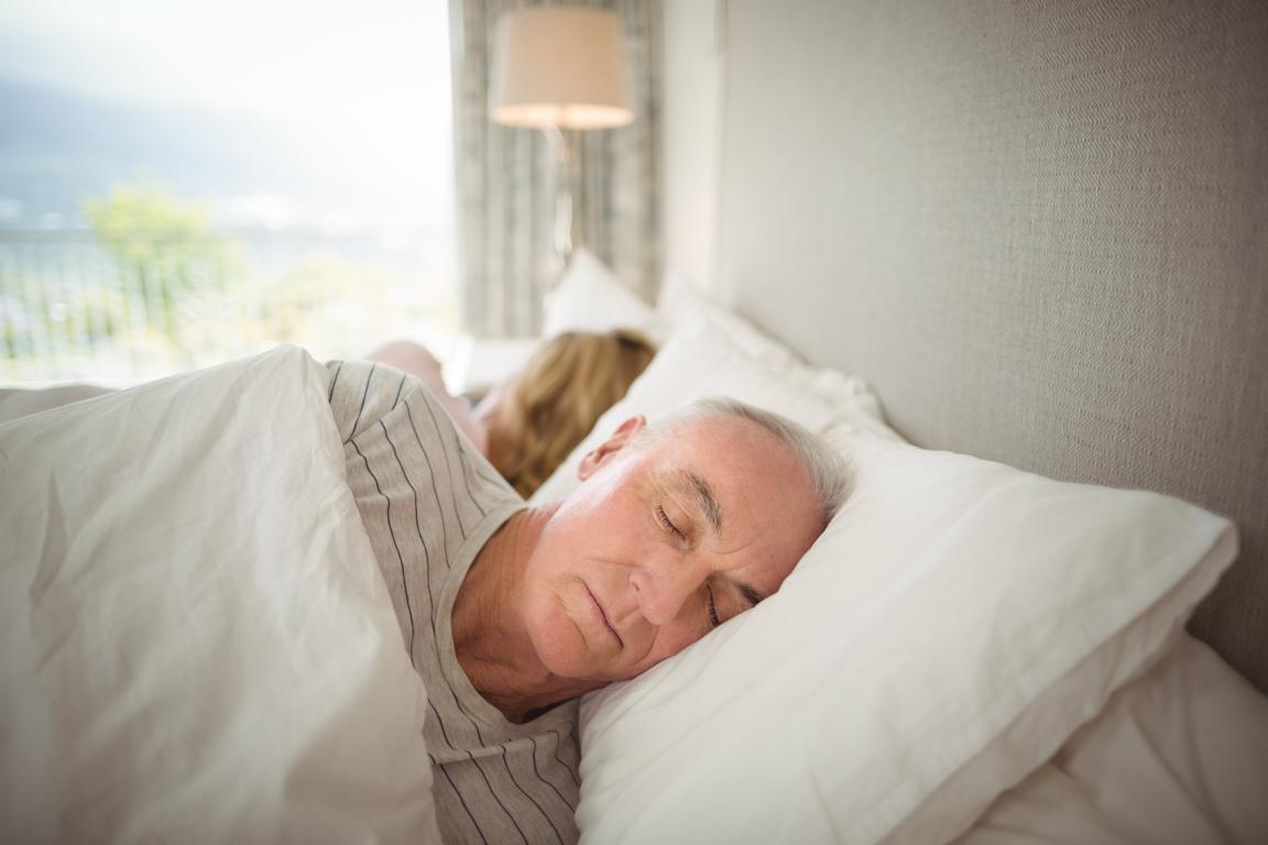 An older man sleeps on his side, a position sometimes recommended to reduce the frequency of apneas and hypopneas (AHI) in mild sleep apnea cases.
