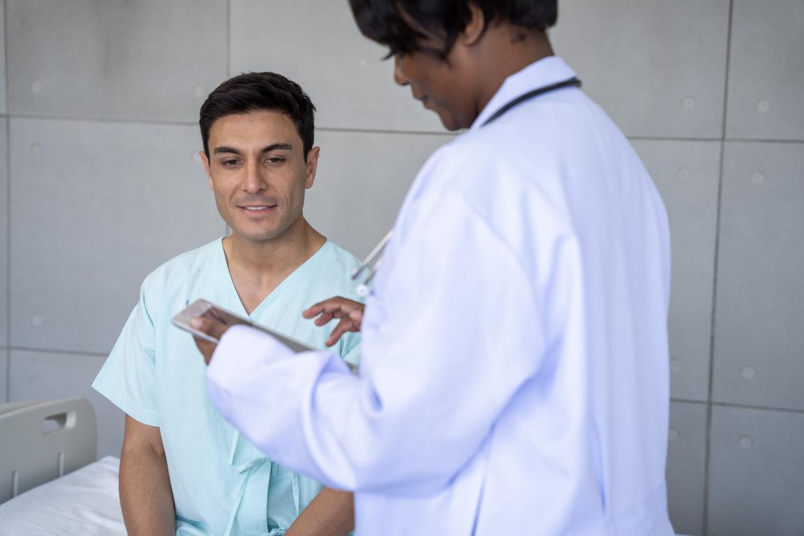 A doctor shows a tablet to a male patient, likely discussing diagnostic results like the Apnea-Hypopnea Index (AHI) from a sleep study