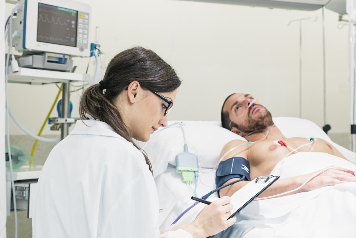  A doctor meticulously reviewing patient data on a clipboard next to a patient in a hospital bed, likely during post-ICD implantation recovery or pre-operative assessment.