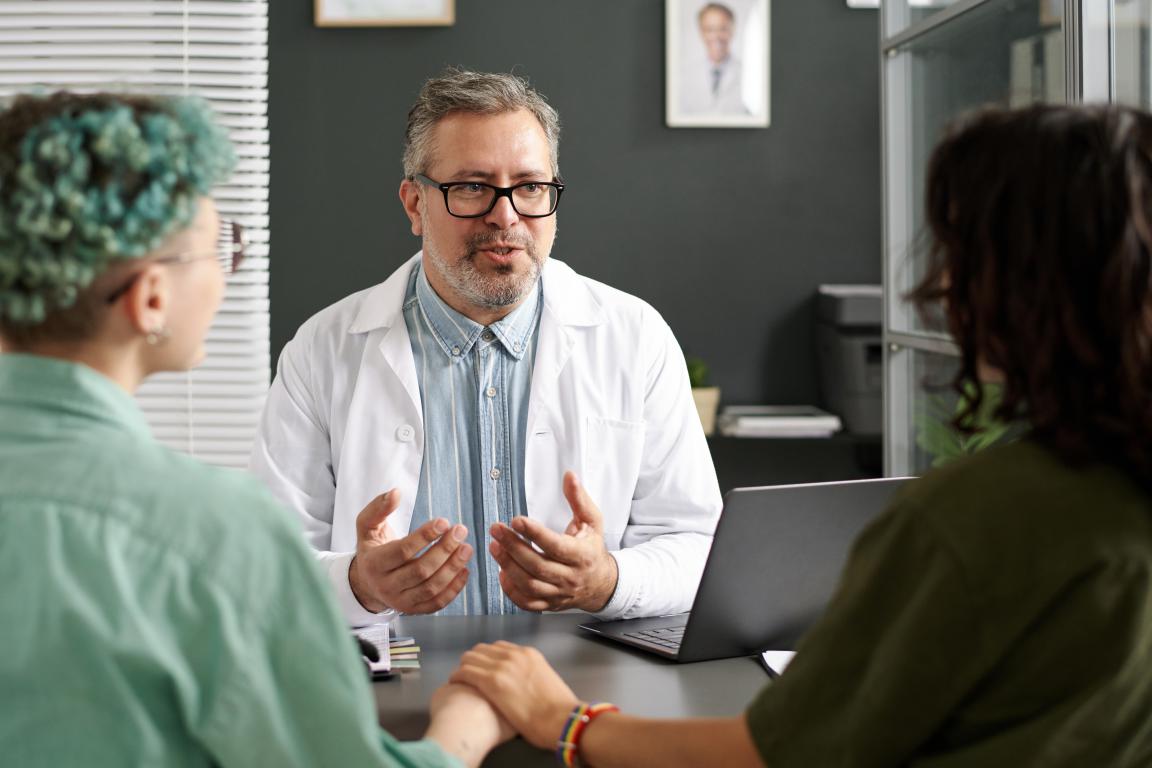 A doctor speaks reassuringly to a patient and their supportive loved one during a hospital visit.