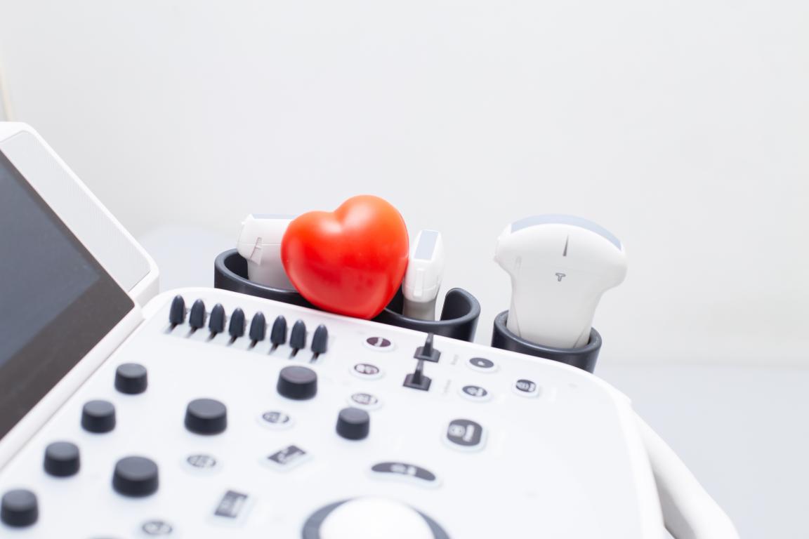 A small red heart model resting on top of an ultrasound machine with various transducers in its holders