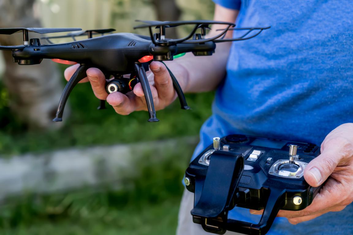 Close-up of hands holding a black drone and a remote controller, with a blurred green background