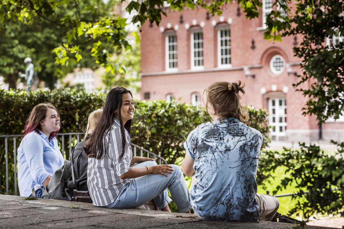 A small group of university students relaxing and chatting informally on campus outdoors near a traditional brick building.