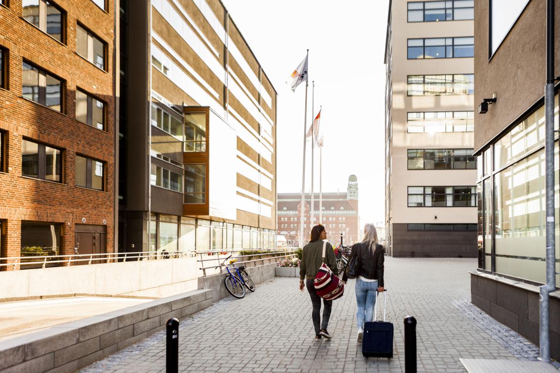 Two students walk across a paved path between modern university campus buildings