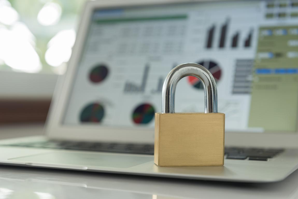 A brass padlock resting on a laptop keyboard with data charts visible on the screen, symbolising data security and encryption.