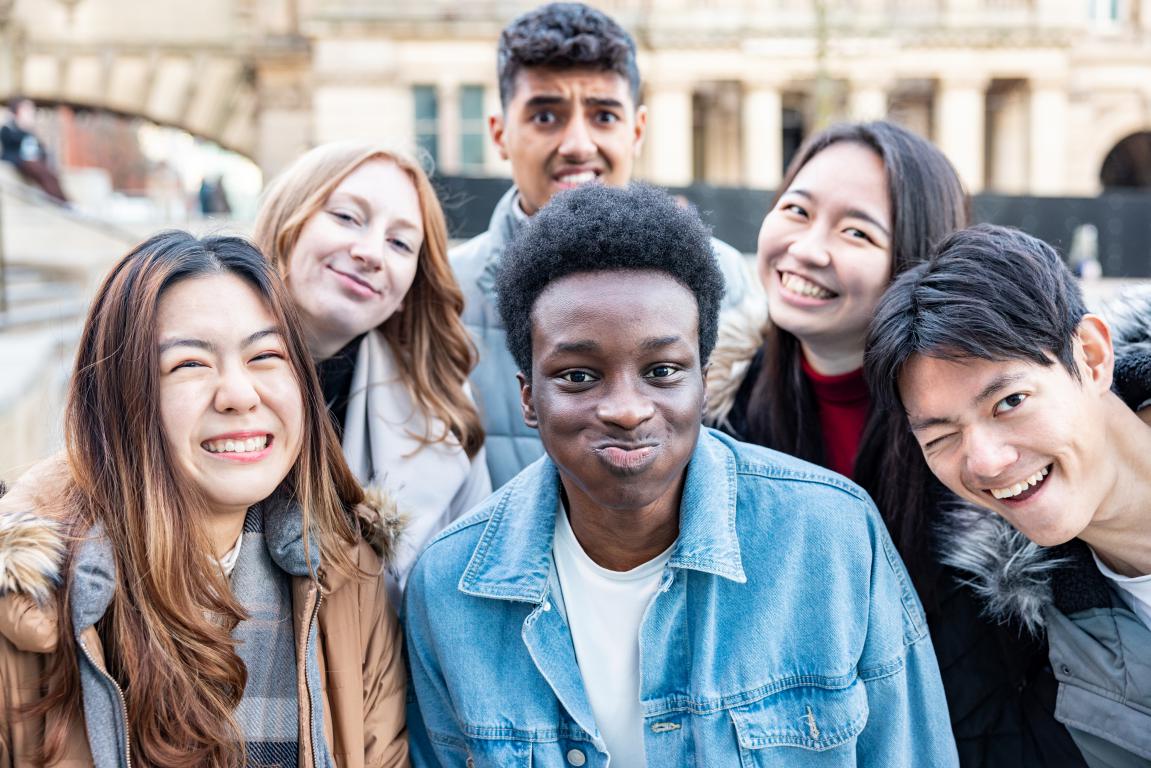 Close-up photo of a diverse group of six happy university students smiling outdoors on campus.
