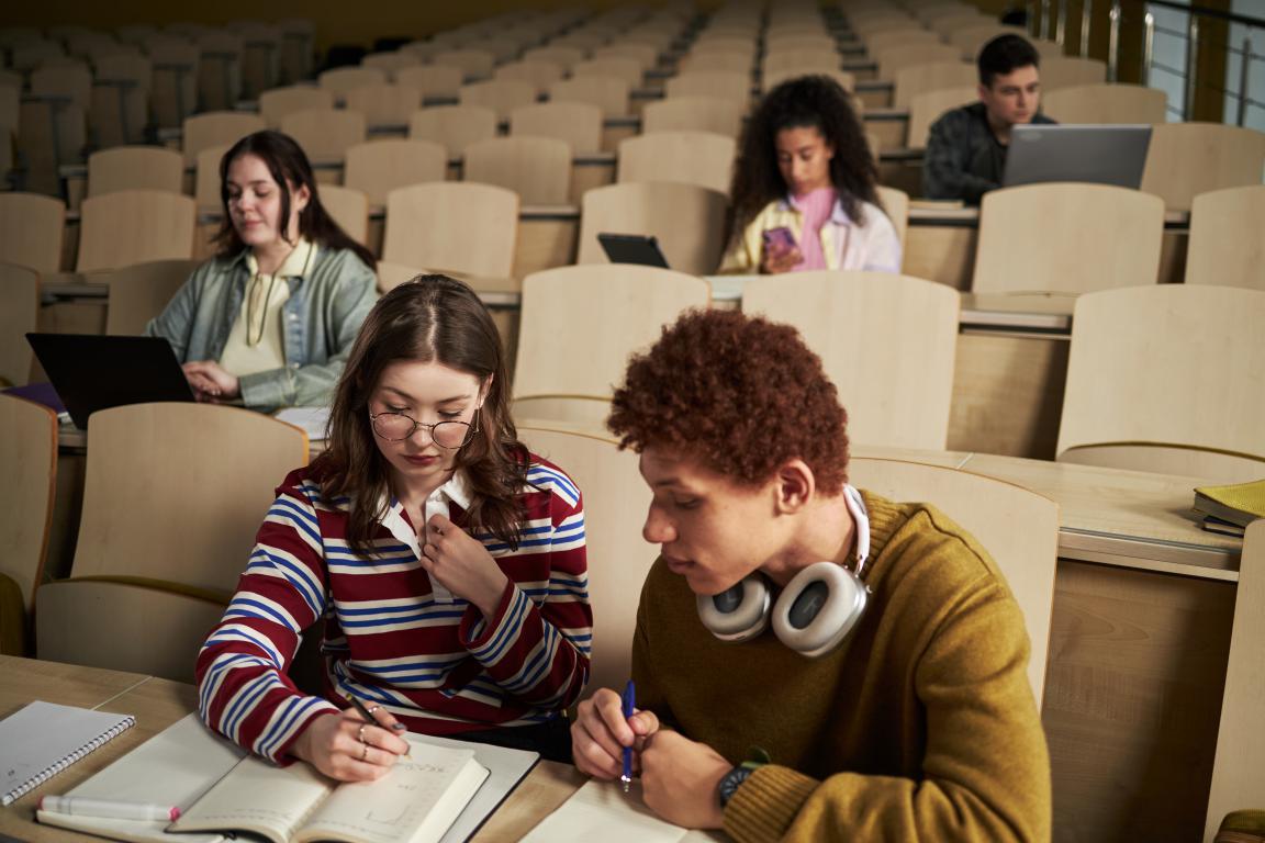 A diverse group of students sitting at desks in a tiered university lecture hall, representing attendance and academic activity.