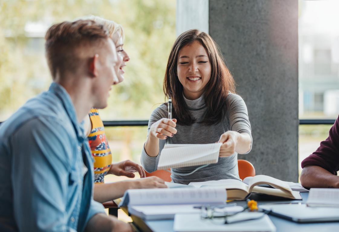 Small group of diverse university students collaborating over notebooks at a study table in a bright, modern campus space.