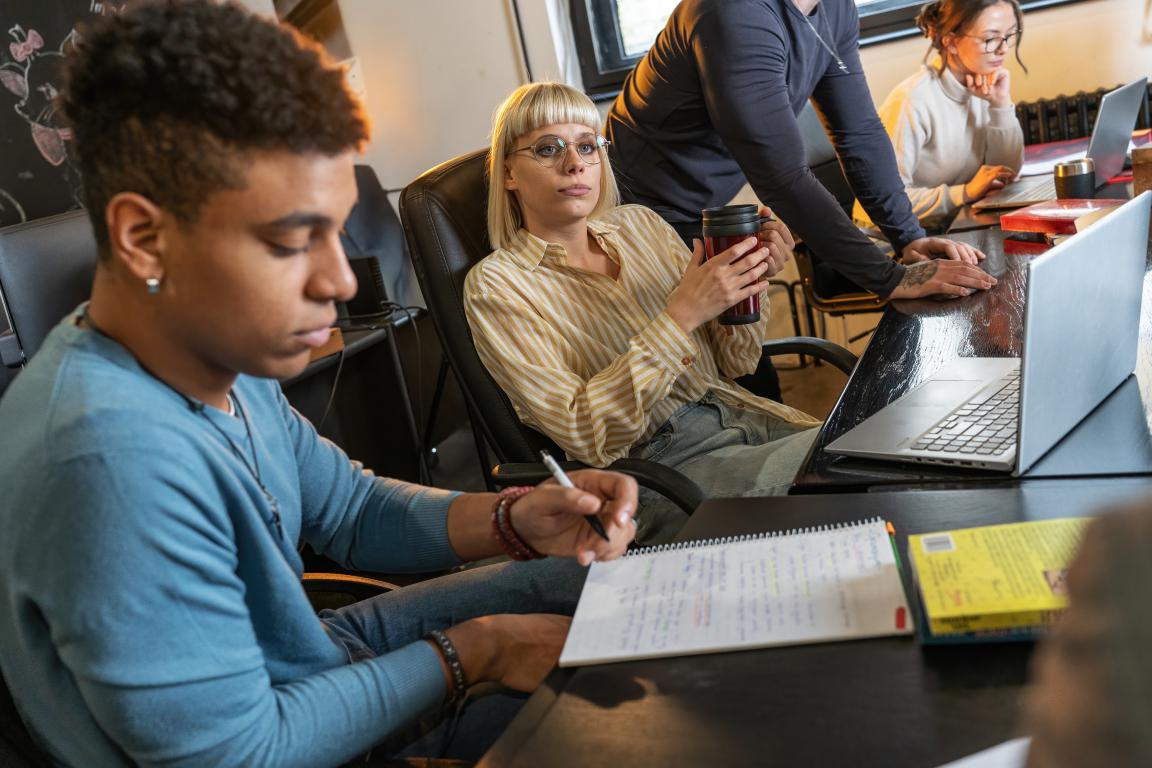 Diverse group of university students studying at a large wooden table in a traditional library, linking to library access data.