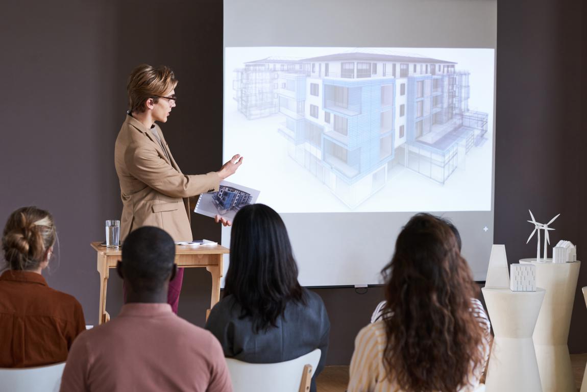 Female instructor presents a 3D building model on screen to learners in a design training course.
