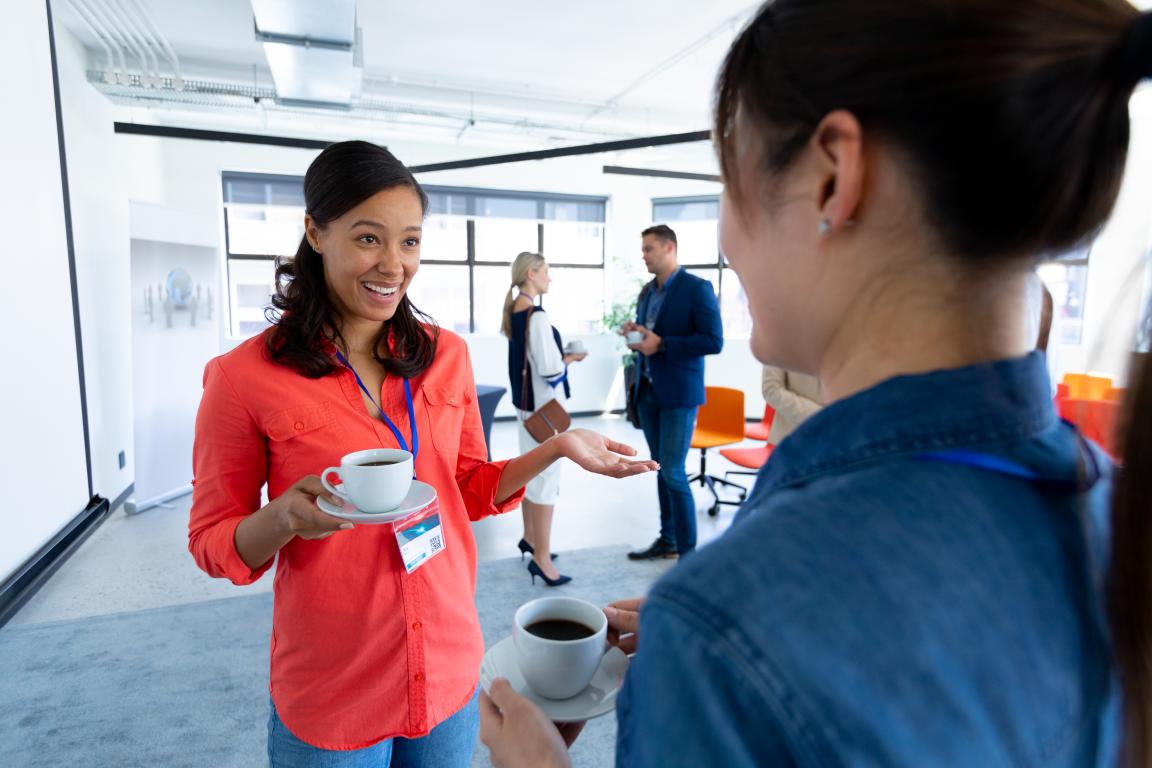 Two early-career professionals smiling and comparing their training ID cards during a coffee-break chat at a work or networking event