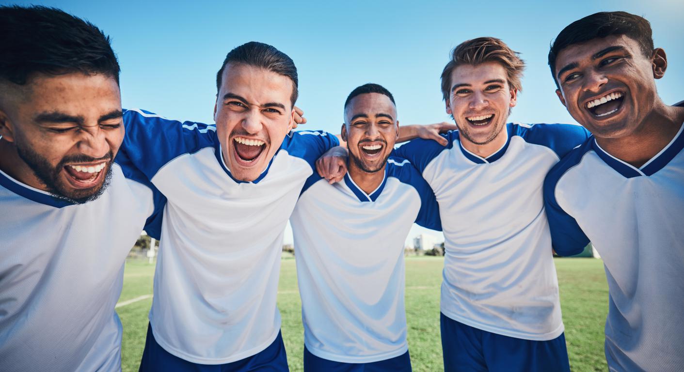Team of diverse adult footballers celebrating together on the pitch
