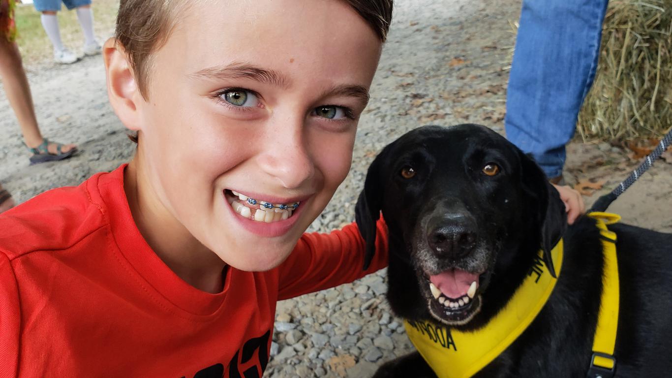 Young boy smiling with his autism assistance dog wearing a yellow vest